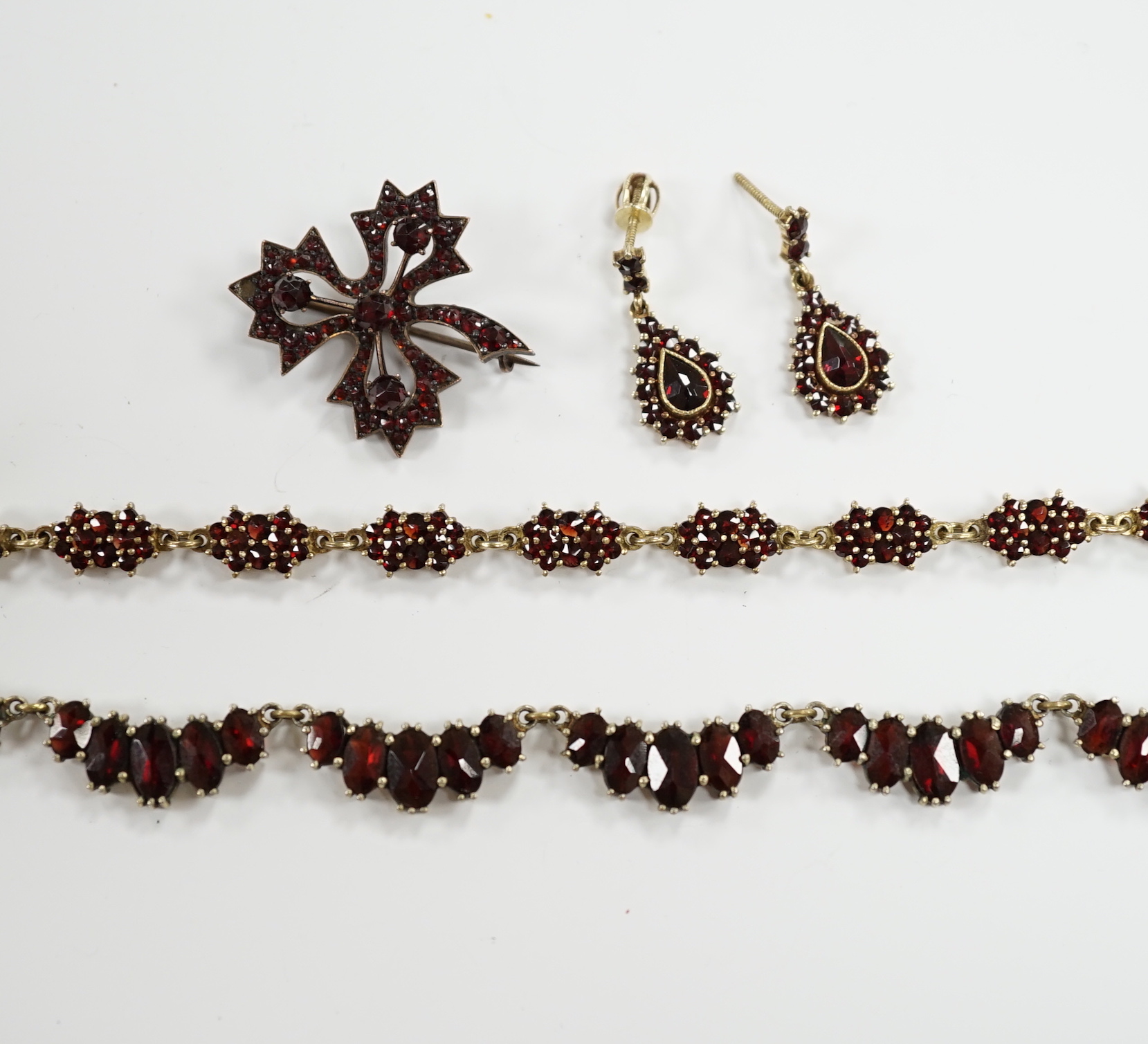 A late 19th/early 20th century Austro-Hungarian 900 gilt white metal and garnet cluster set fringe necklace, 43cm, a similar bracelet and pair of earrings and a garnet paste set brooch.